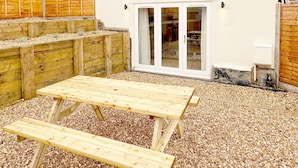 Une maison à deux étages dotée d’un patio comprenant une table et des bancs en bois.