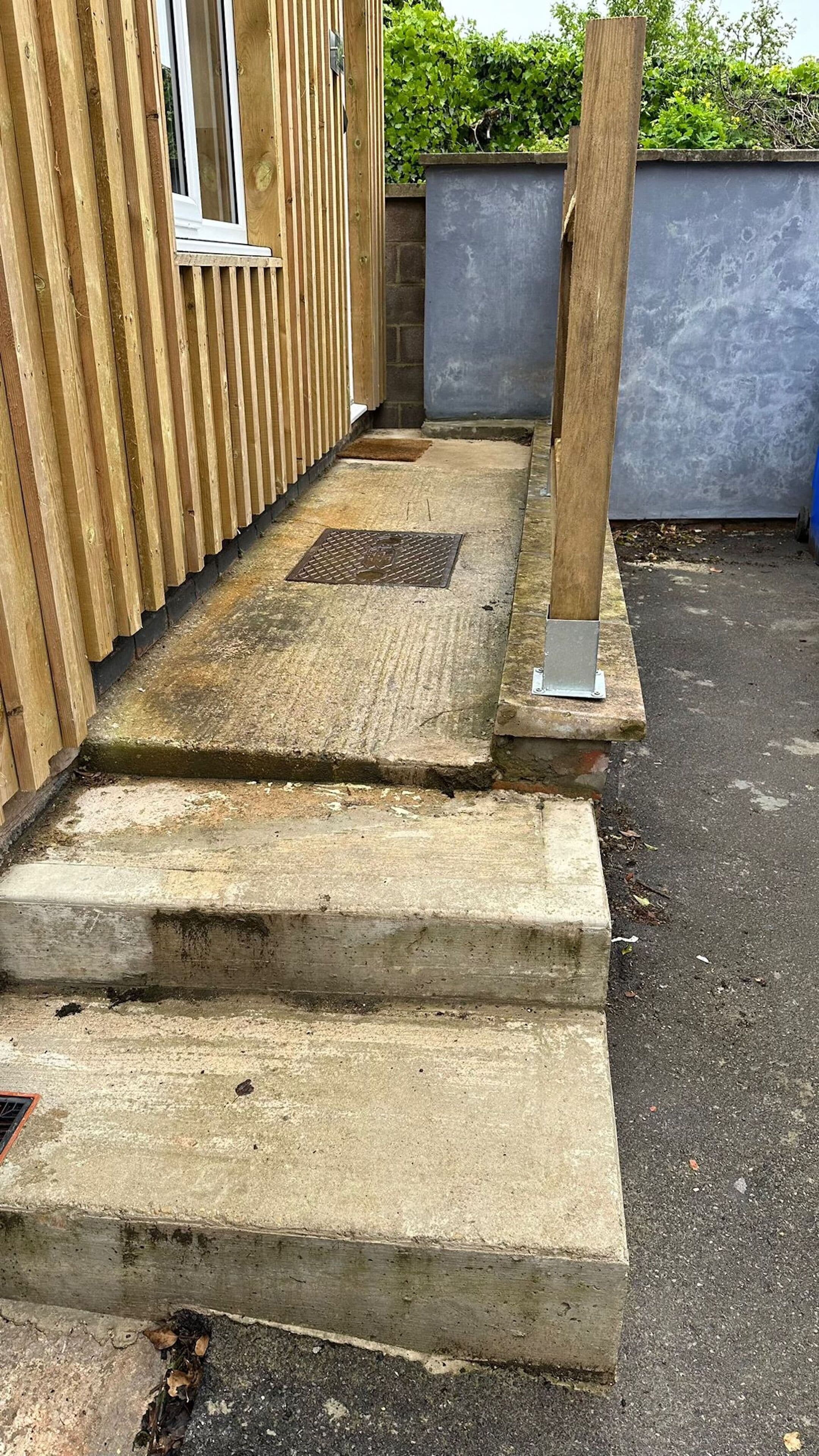 A concrete staircase leading to a wooden door, with a metal handrail on the right.
