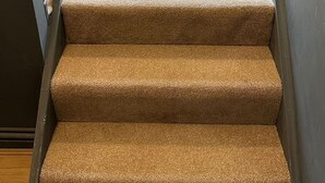 Un escalier dont les marches sont recouvertes d’une moquette beige, menant à une porte ouverte.