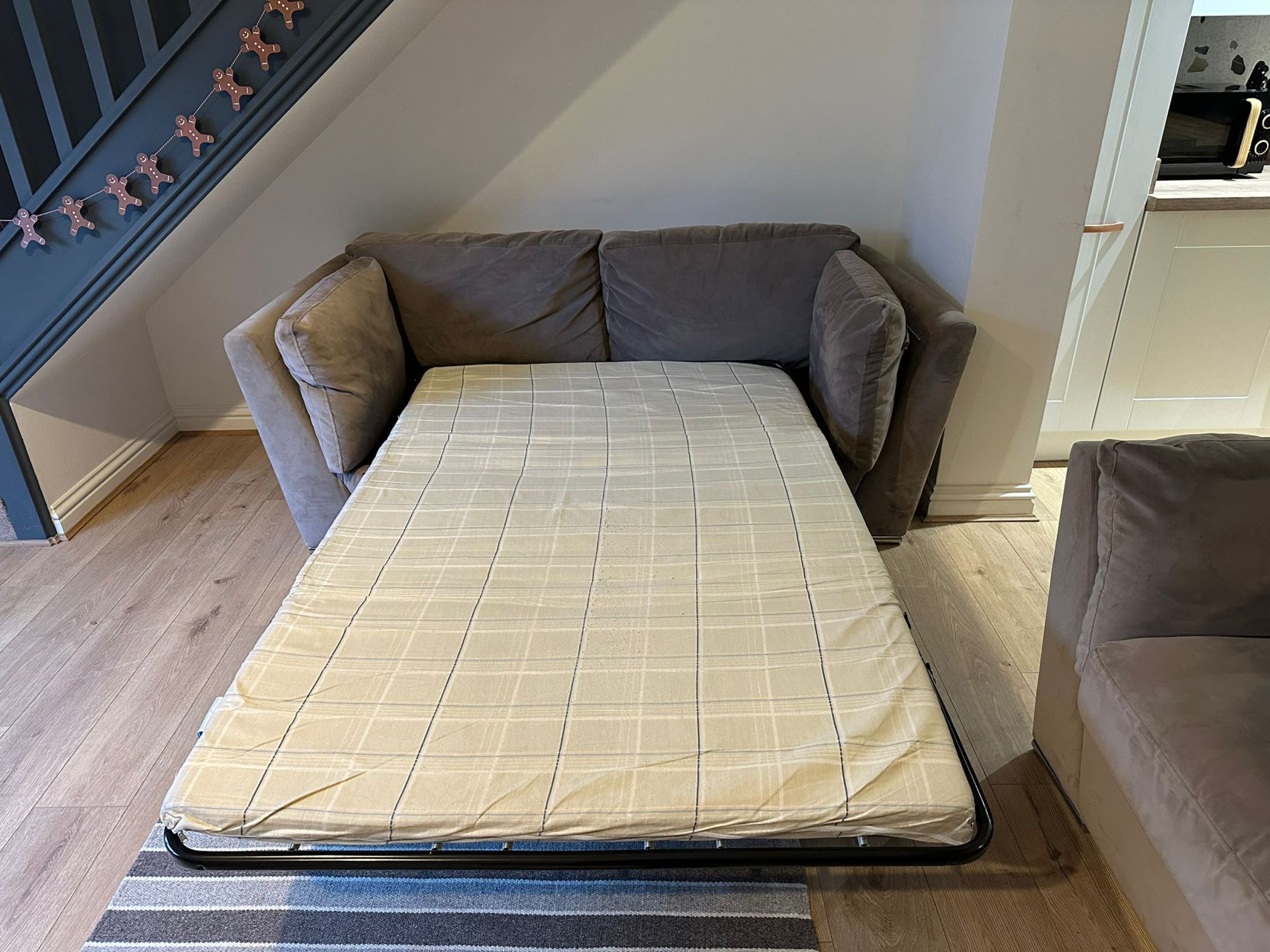 En liten säng med ett rutigt madrassöverdrag i ett rum med en trappa och en soffa.