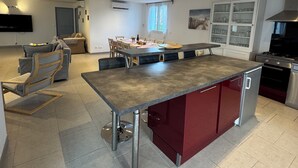 Una cocina moderna con una isla central, una zona de comedor con mesa y sillas, un horno empotrado y un televisor montado en la pared.