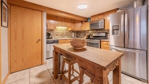 Una cucina moderna con mobili in legno, un frigorifero in acciaio inossidabile, un forno a microonde e una grande isola di legno con sgabelli.