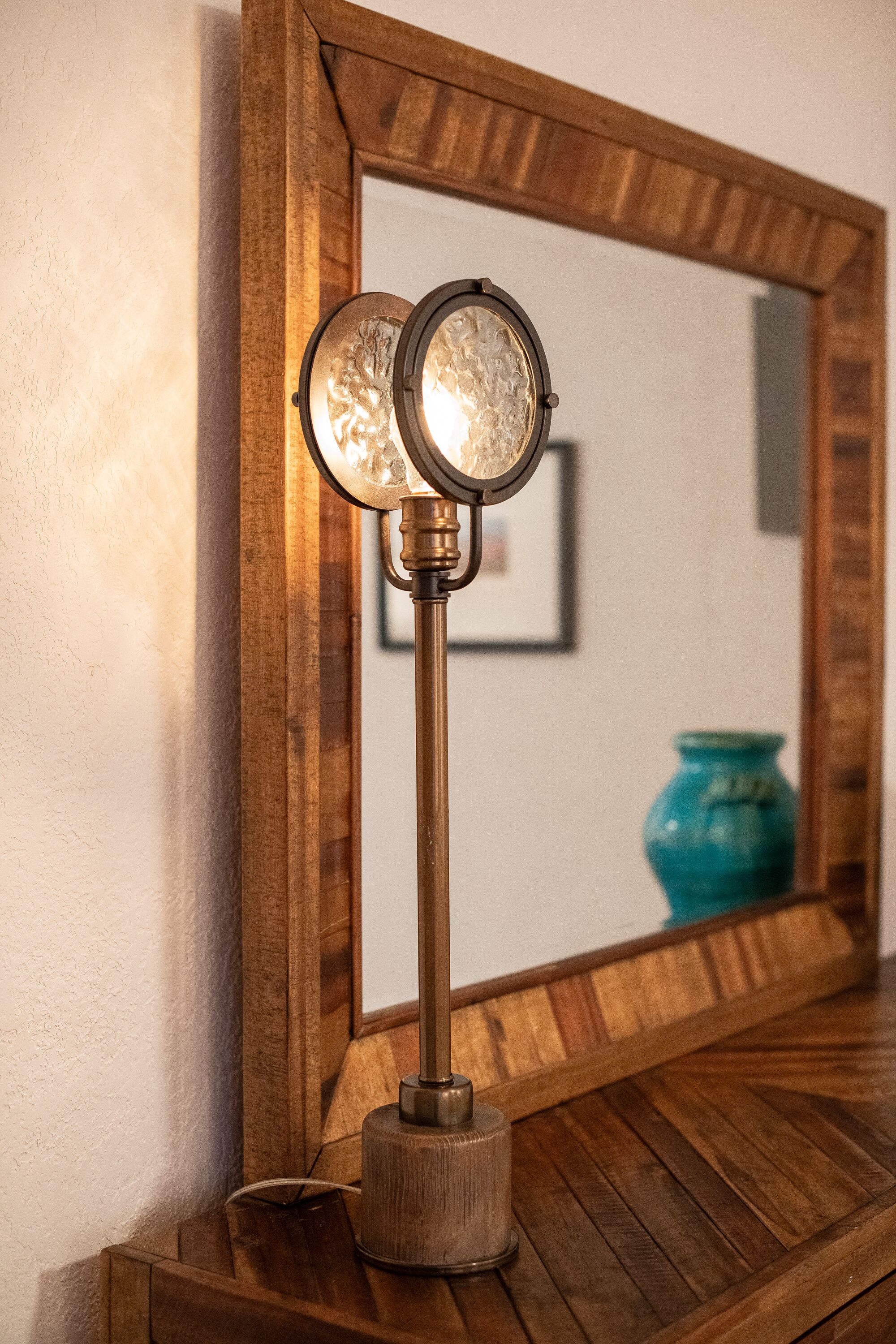 A wooden-framed mirror with a round, vintage-style lamp in front of it.