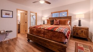 Una camera da letto con un letto di legno, una ventola a soffitto, un comodino con una lampada e un pavimento in legno.