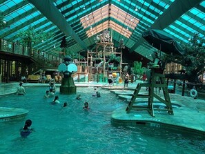 Un parc aquàtic interior amb una gran piscina central, diverses zones de jocs i un sostre de vidre elevat.