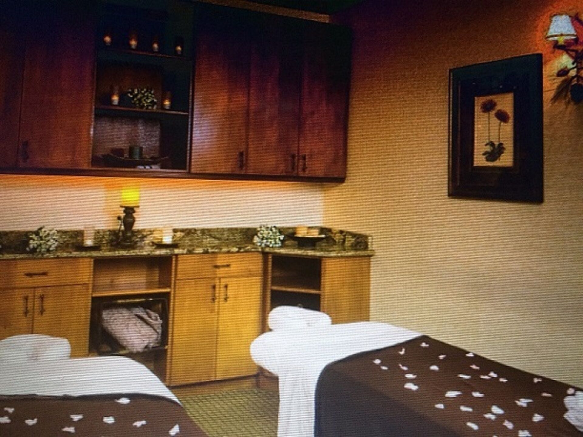 Et hotelværelse med et træskab, et lille bord med en lampe og et billede i ramme på væggen.