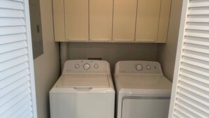 A compact laundry room with two front-loading washing machines and beige cabinets above. - Marvel GulfCondo - One Bedroom Hotel, Sleeps 4 (Gulfport)