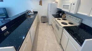 A compact kitchen with a black countertop, white cabinets, a stove, a microwave, and a refrigerator. - Marvel GulfCondo - One Bedroom Hotel, Sleeps 4 (Gulfport)