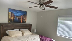 A bedroom with a bed, a ceiling fan, a window with blinds, and a painting on the wall. - Marvel GulfCondo - One Bedroom Hotel, Sleeps 4 (Gulfport)