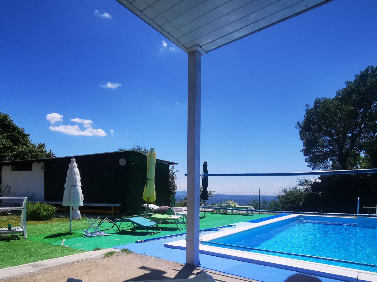 A swimming pool with a clear blue sky, a covered seating area, and a building in the background.