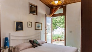 A bedroom with a bed, a bedside table, a window, and a door leading to an outdoor area.