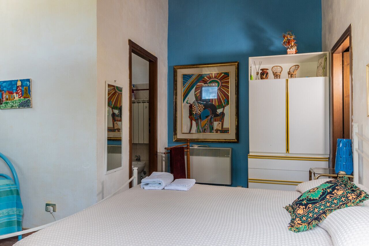A bedroom with a bed, a wardrobe, a mirror, and a painting on the wall.