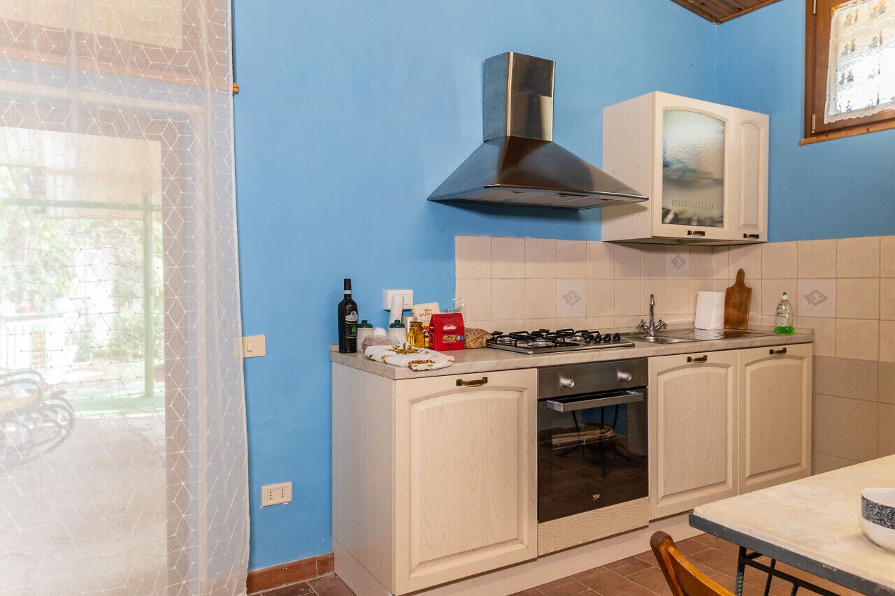 La cuisine est équipée d’une cuisinière à gaz, d’un four et d’un four à micro-ondes. Une fenêtre offre une vue sur la verdure environnante.