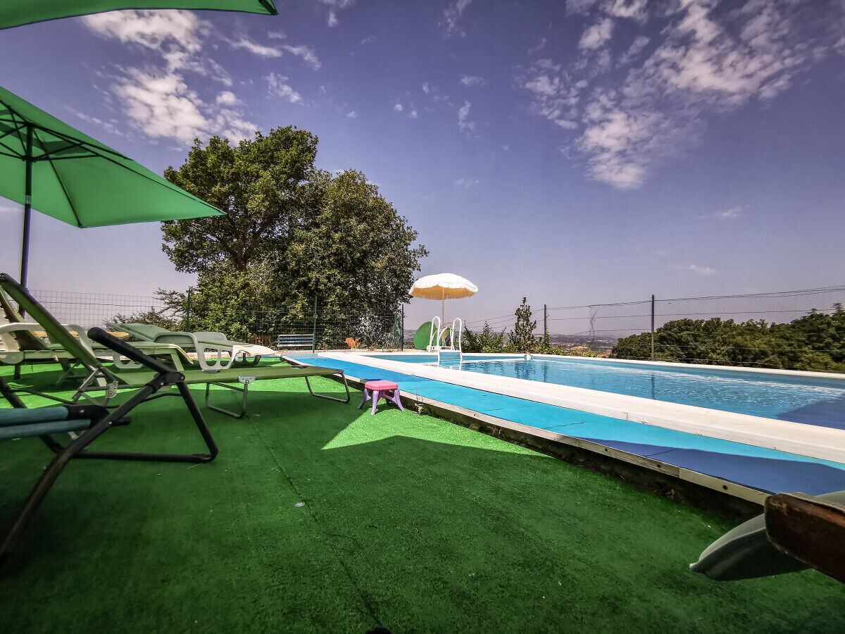 Une piscine avec une zone recouverte d’un gazon artificiel vert, un petit tabouret rose et un parasol vert.