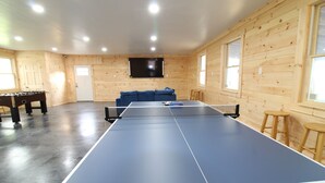 Ein Tischtennistisch in einem Raum mit Holzwänden, einer Couch und einem an der Wand montierten Fernseher.