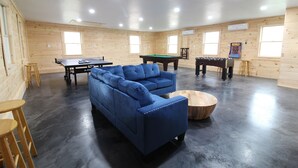 Ein Zimmer mit einem blauen Sofa, einem Billardtisch, einem Kicker und einem Tischtennistisch.