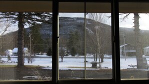 Blick durch ein Fenster auf eine verschneite Landschaft mit Bäumen und einem Haus.