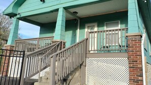 A two-story house with a green exterior, a front porch with a railing, and a staircase leading to the entrance. - Experience football fun! 4BR/2Bath Independence retreat near Arrowhead (Sugar Creek)