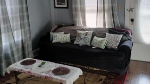 A living room with a dark-colored sofa, a coffee table with a floral tablecloth, and a patterned rug. - Experience football fun! 4BR/2Bath Independence retreat near Arrowhead (Sugar Creek)