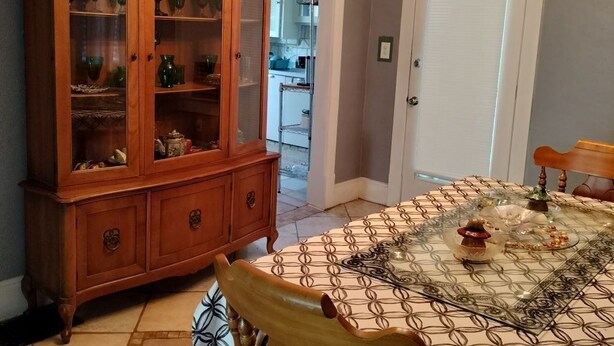 A dining area with a patterned tablecloth, a wooden cabinet with glass doors, a wall clock, and a modern chandelier. - Experience football fun! 4BR/2Bath Independence retreat near Arrowhead (Sugar Creek)