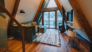 Une chambre à coucher confortable, aménagée en mezzanine, avec un plafond en pente, un canapé vert, une table basse blanche et une grande fenêtre donnant sur l’extérieur.
