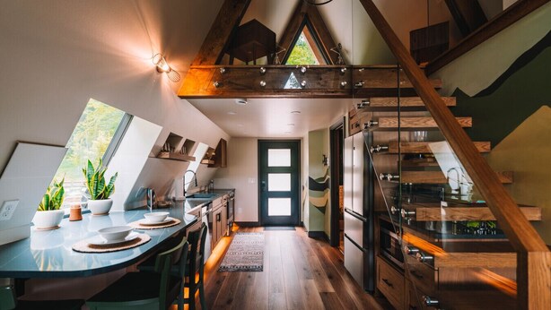 Une cuisine moderne avec un escalier en bois, un coin repas avec une table et des chaises, et une vue par la fenêtre.
