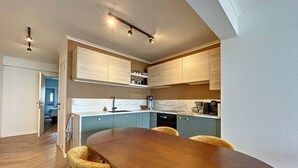 A modern kitchen with a wooden dining table and chairs, built-in cabinets, and a visible kitchen island. - Flat Las Vegas - Seaview (Middelkerke)