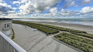 A beach view with a building on the left, a paved walkway, and grassy areas. - Flat Las Vegas - Seaview (Middelkerke)