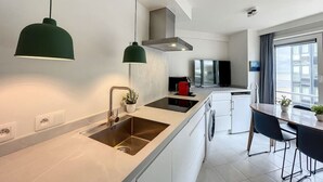 A modern kitchen with a large island, stainless steel appliances, and pendant lighting. - Flat Vendome - Studio with seaview (Middelkerke)