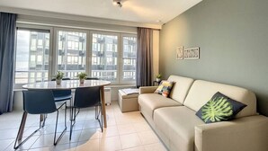 A modern living room with a sofa, a dining table with chairs, and a large window with curtains. - Flat Vendome - Studio with seaview (Middelkerke)
