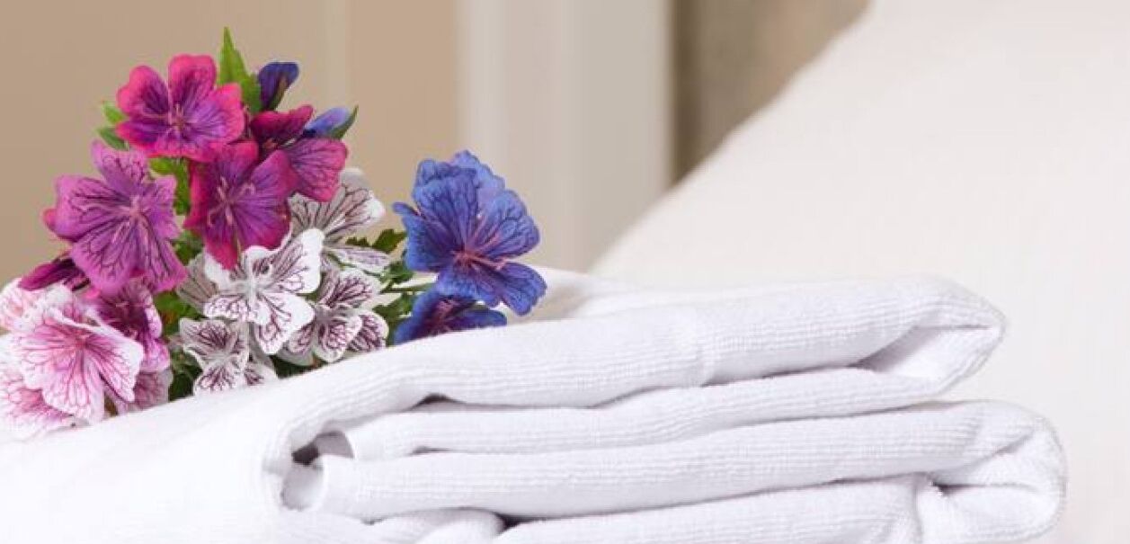 Une serviette blanche soigneusement pliée et un bouquet de fleurs sur un lit.