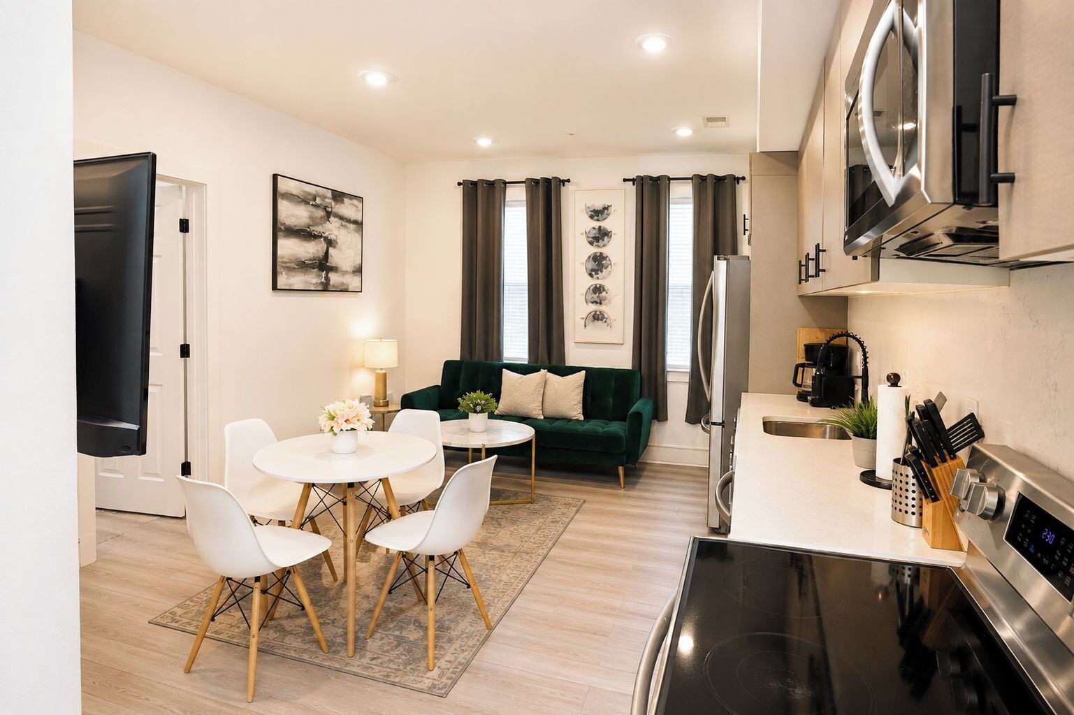Un salon moderne avec un canapé vert, une table à manger avec des chaises, un téléviseur à écran plat et un coin cuisine équipé d’une cuisinière et d’un réfrigérateur.