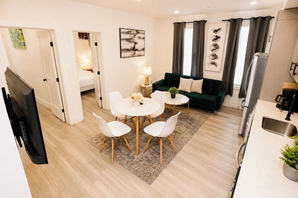 Ein modernes Wohnzimmer mit Essbereich, einer Couch, einer Kaffeemaschine und einem Fernseher.
