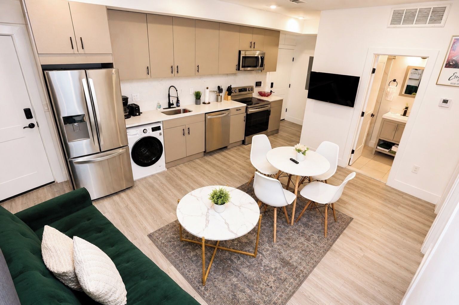 Une cuisine moderne équipée d’appareils électroménagers en acier inoxydable, un coin repas avec des chaises blanches et un canapé vert.