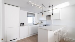 A modern kitchen with white cabinetry, a central island, pendant lighting, and a window with blinds.