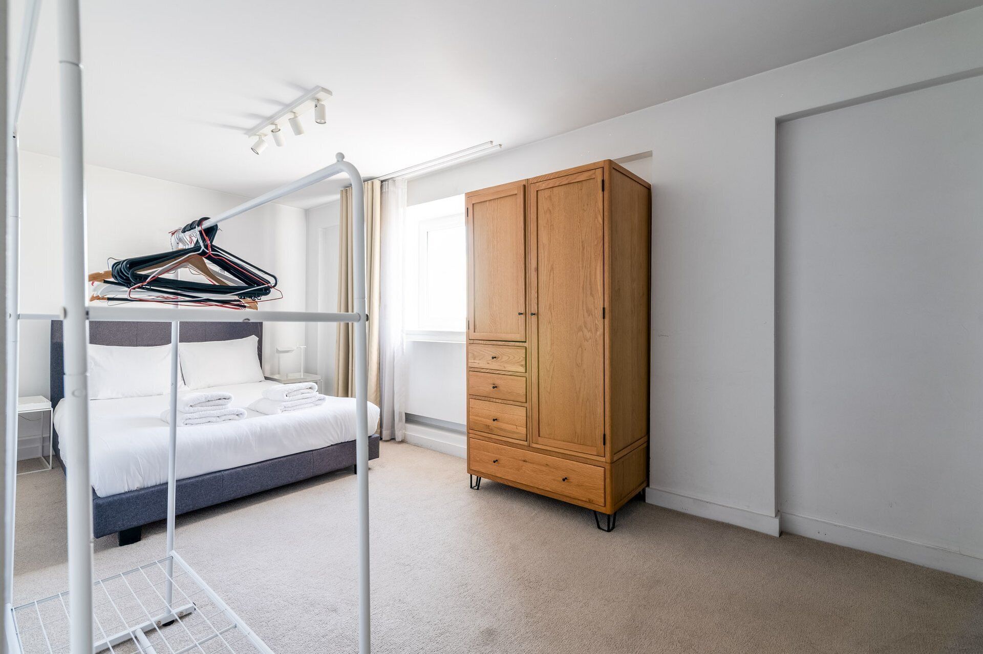 A bedroom with a bunk bed, a wooden wardrobe, and a hanging clothes rack.