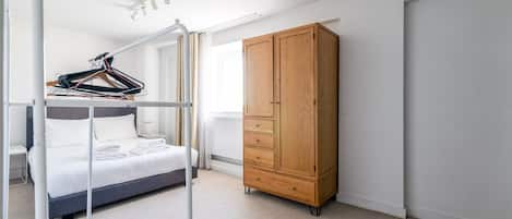 Un dormitorio con literas, un armario de madera y una percha para ropa.