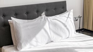 A bed with a grey upholstered headboard and white bedding.
