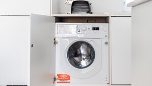 A front-loading washing machine in a white utility room with a control panel and a label indicating a 10-year parts guarantee.