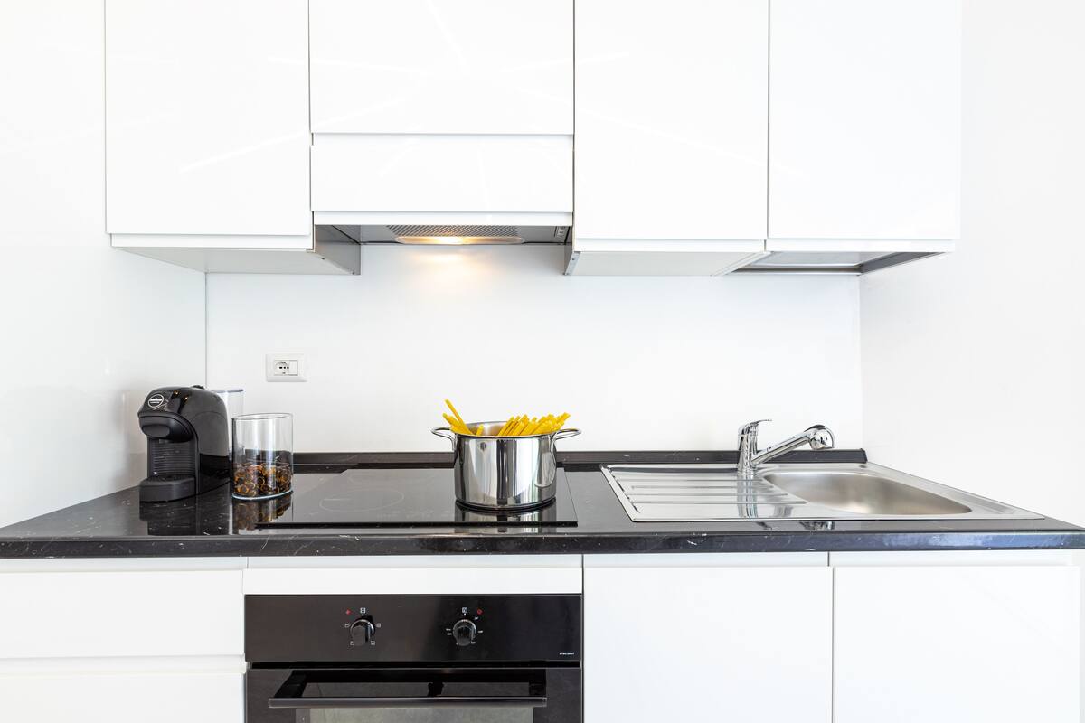 A modern kitchen with white cabinets, a black countertop, a coffee machine, a glass of water, and a pot of French fries.