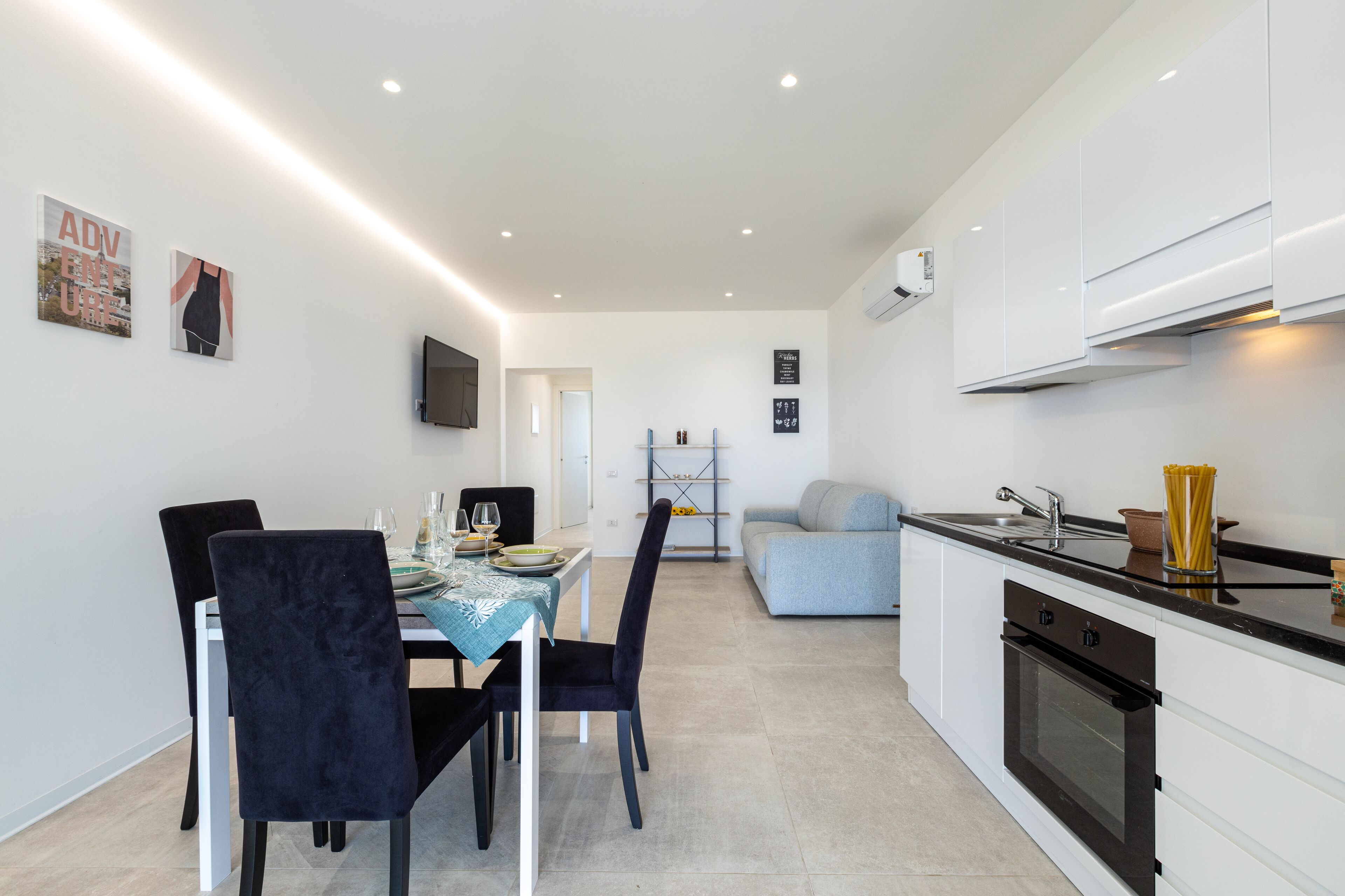 Una cocina moderna con armarios blancos, encimera negra y un comedor con una mesa preparada para dos personas.