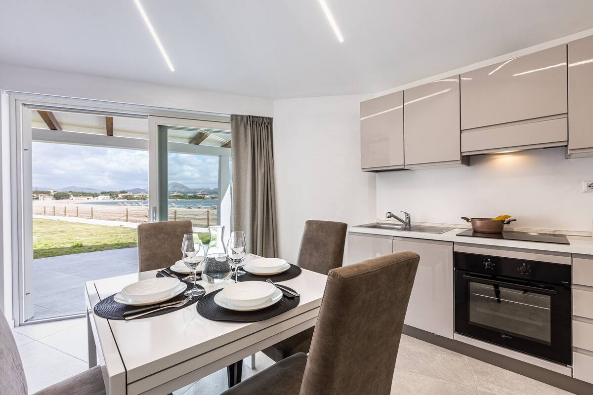 A modern kitchen with a dining area, large windows, and a view of the outdoors.