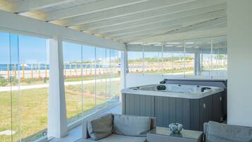 A modern room with a glass wall, a hot tub, and a seating area with cushions.