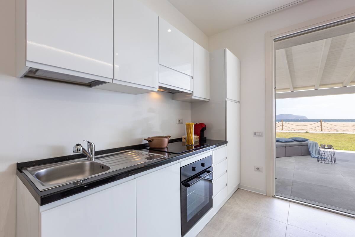 A modern kitchen with white cabinets, a black countertop, and a stainless steel sink.
