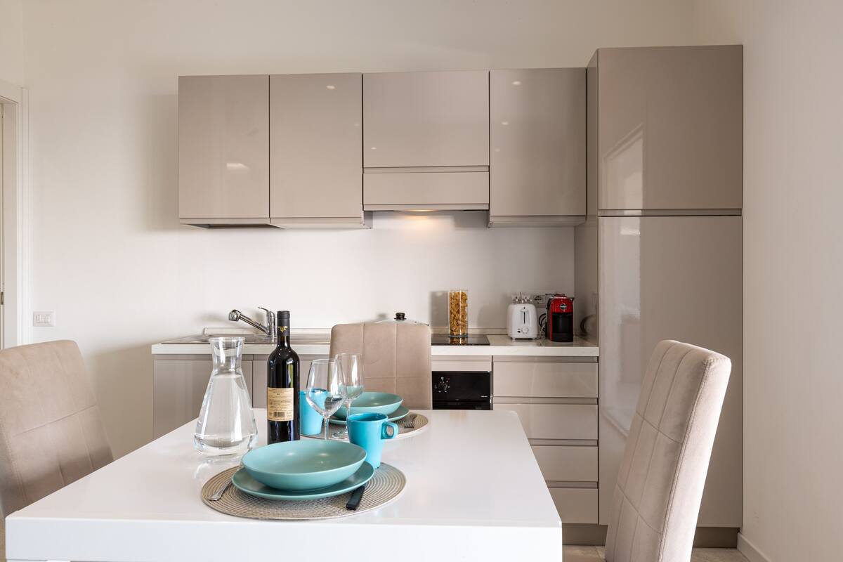 A modern kitchen with white cabinets, a dining table set with blue plates, and a coffee machine.
