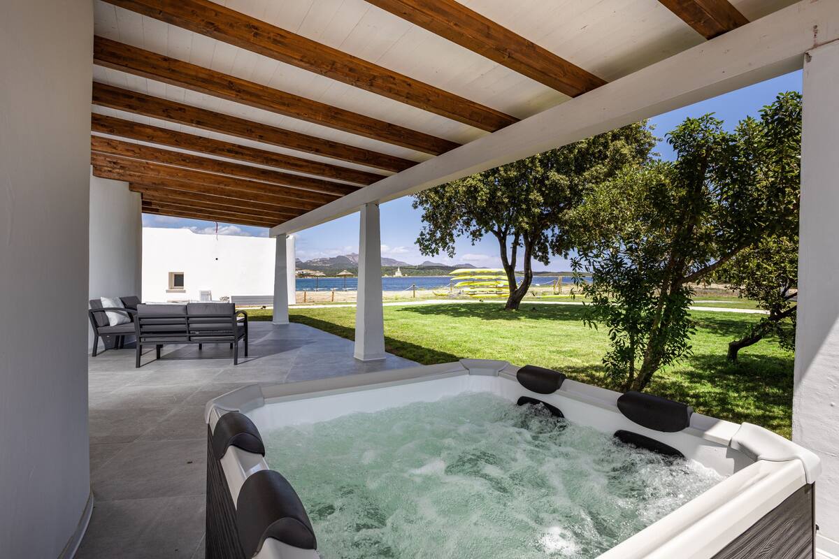 A hot tub under a wooden pergola with a view of a grassy area and a body of water.