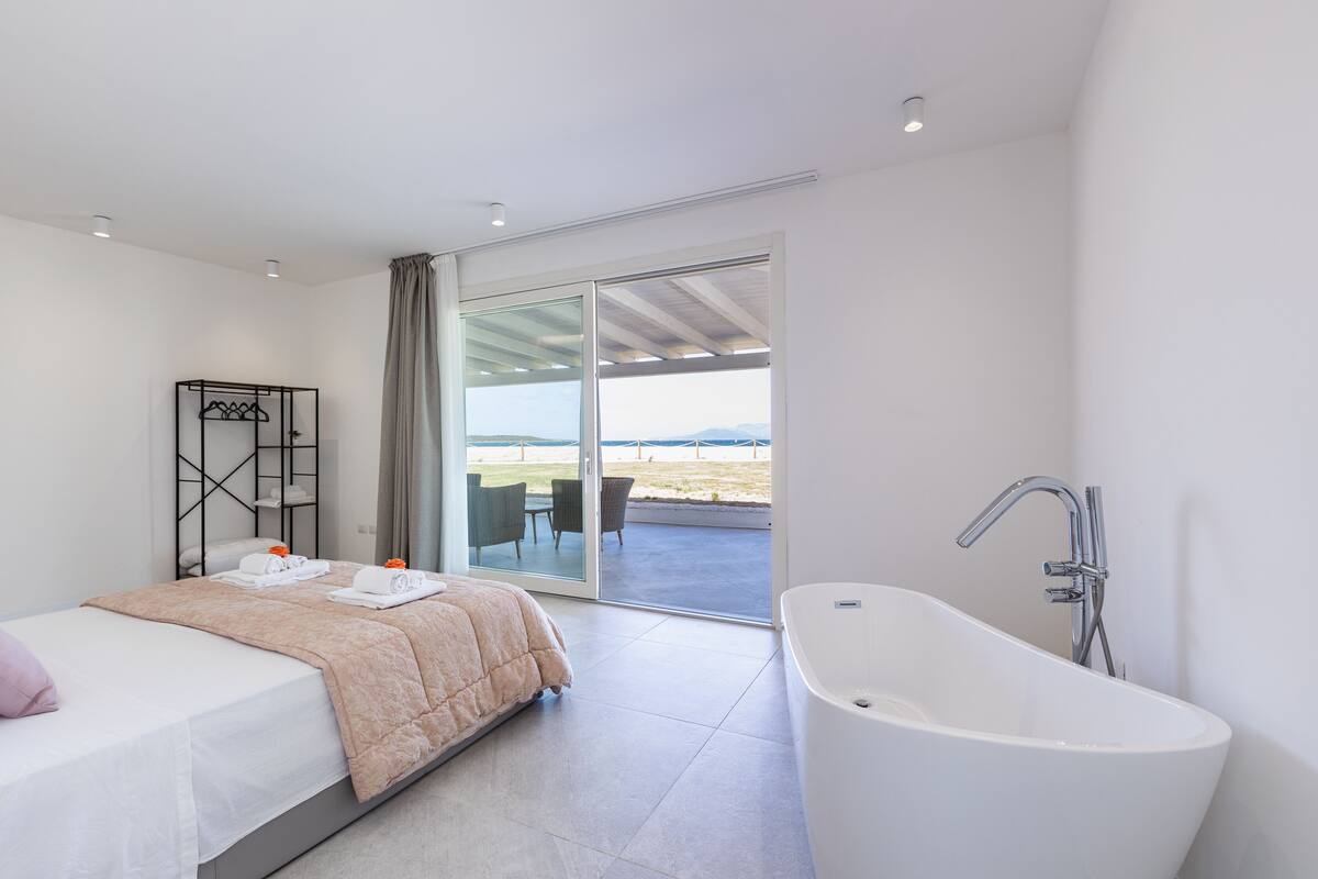 A modern bedroom with a large bed, a bathtub, and a sliding glass door leading to an outdoor area.