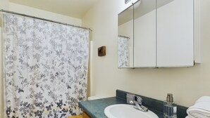 Een badkamer met een gordijn met bloemenprint, een wit toilet, een wastafel met een groen aanrechtblad en een spiegel boven de wastafel.