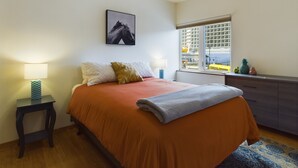 Een slaapkamer met een bed, een nachtkastje, een raam met uitzicht en een aan de muur hangend schilderij.