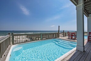 A pool with a wooden deck, a wooden railing, and a view of the ocean.